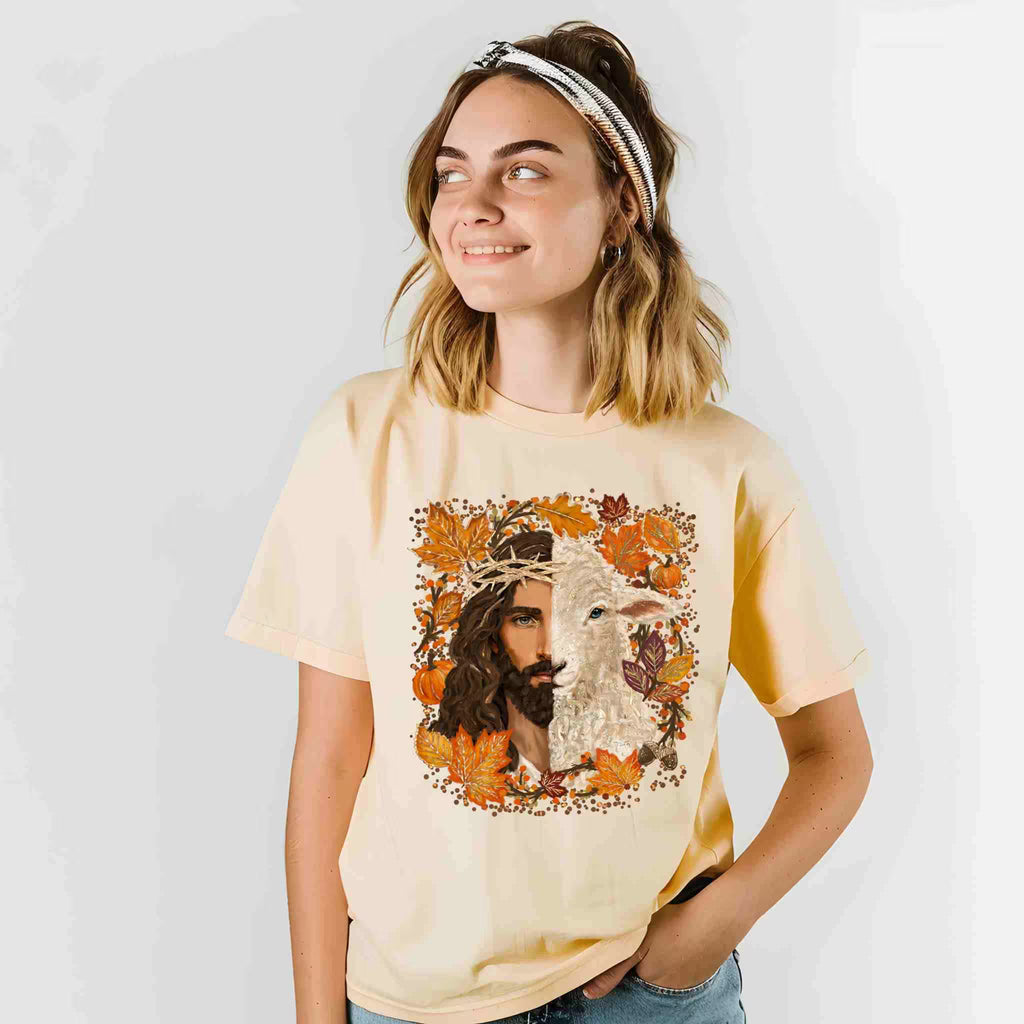 Woman wearing a beige t-shirt with a graphic design of a man and a lamb surrounded by autumn leaves.