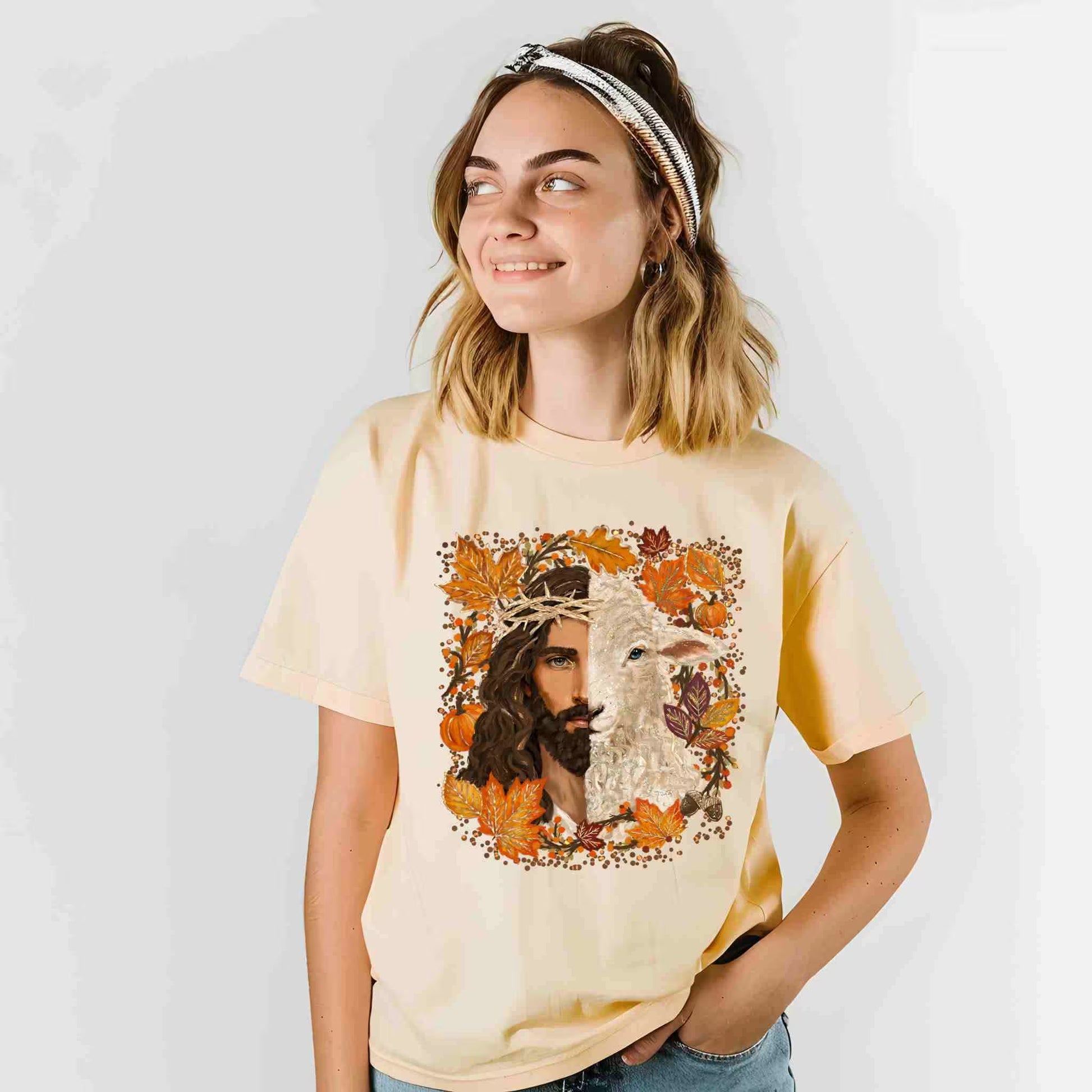 Woman wearing a beige t-shirt with a graphic design of a man and a lamb surrounded by autumn leaves.