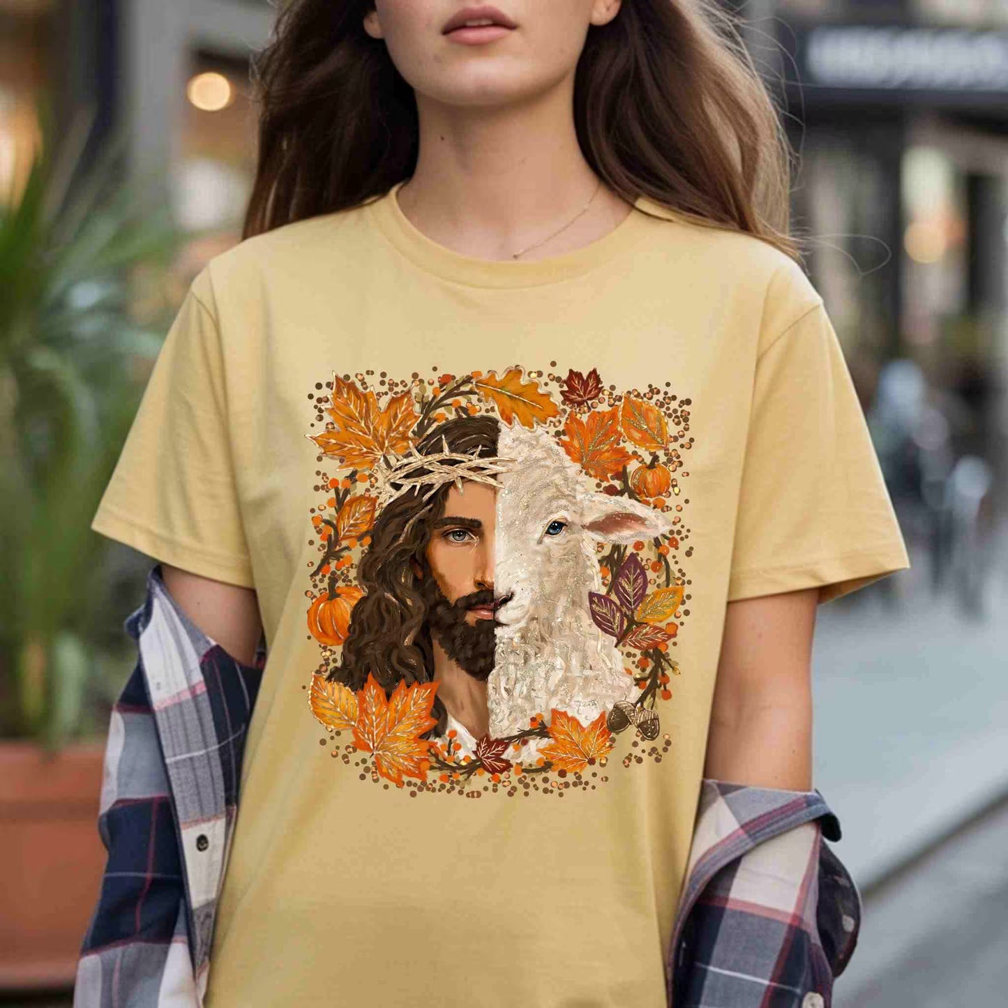 Person wearing a yellow t-shirt with a graphic design of Jesus and a lamb surrounded by autumn leaves.