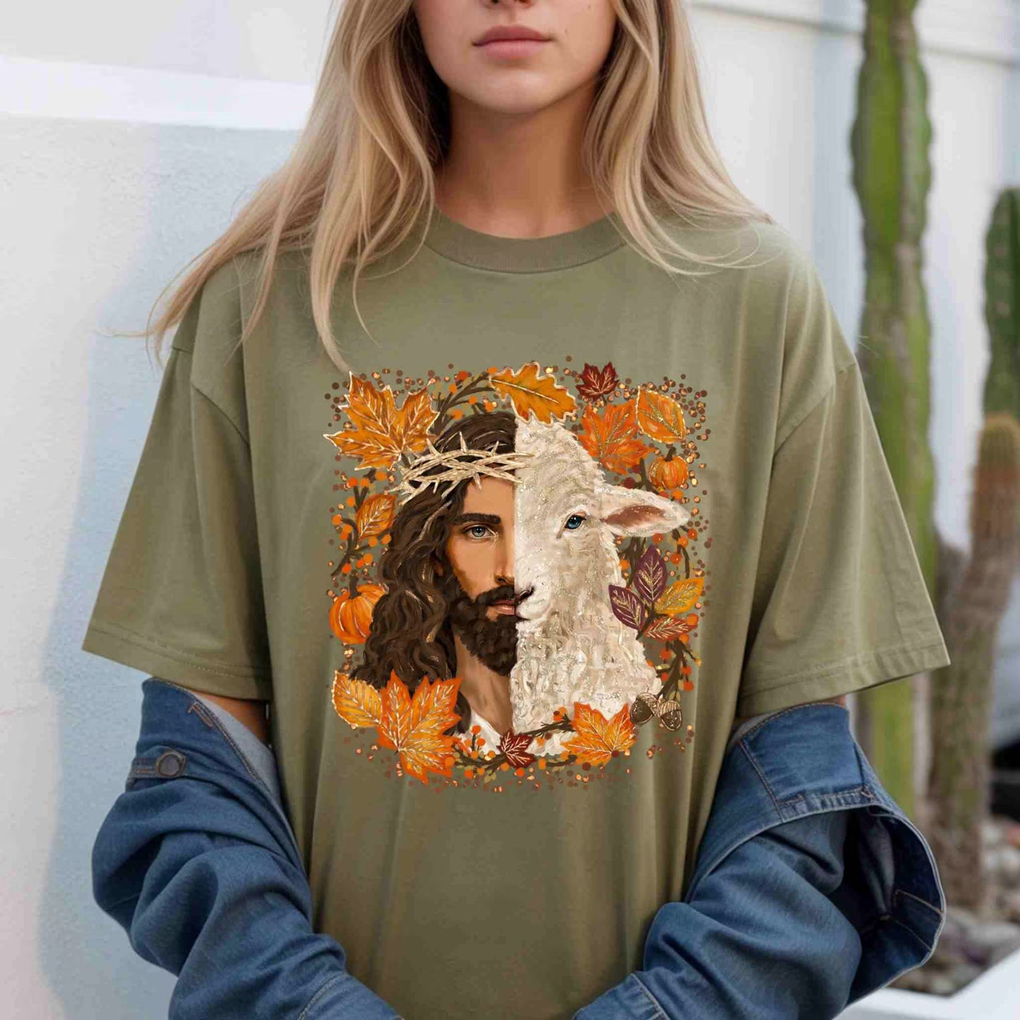 Person wearing a green t-shirt with a graphic design of Jesus and a lamb, surrounded by autumn leaves and pumpkins.