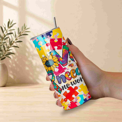 A hand holds Becca's Banging Designs LLC’s Autism Awareness Love Needs No Words Tumbler—a 20oz cup with puzzle pieces and a sunflower, perfect as an autism support gift. A metal straw is in the tumbler, with a small plant vase behind it.