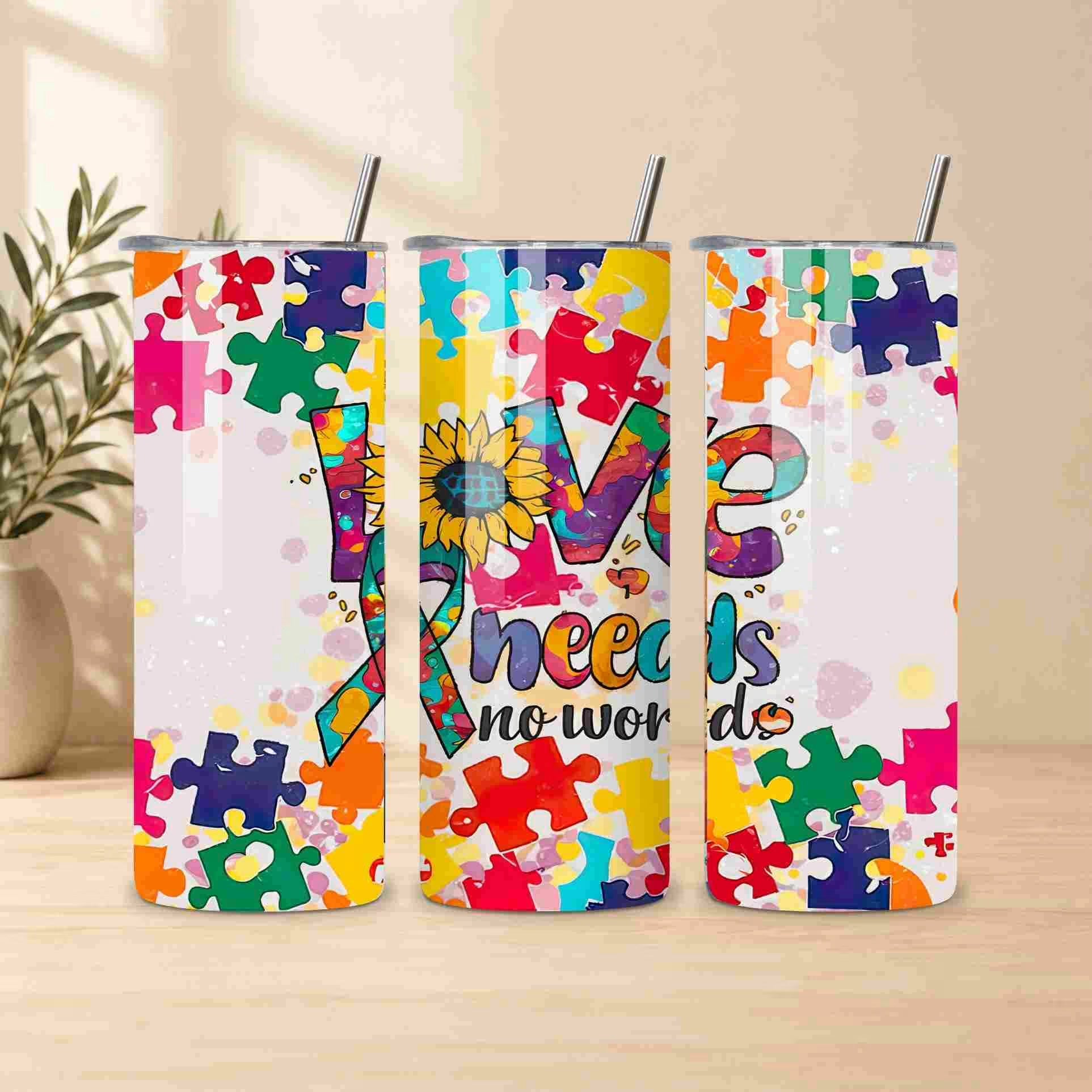 Three Autism Awareness Love Needs No Words 20oz tumblers by Becca's Banging Designs LLC, with puzzle piece and sunflower "O" designs, make a perfect support gift. The cups are displayed on a table with a plant in the background.