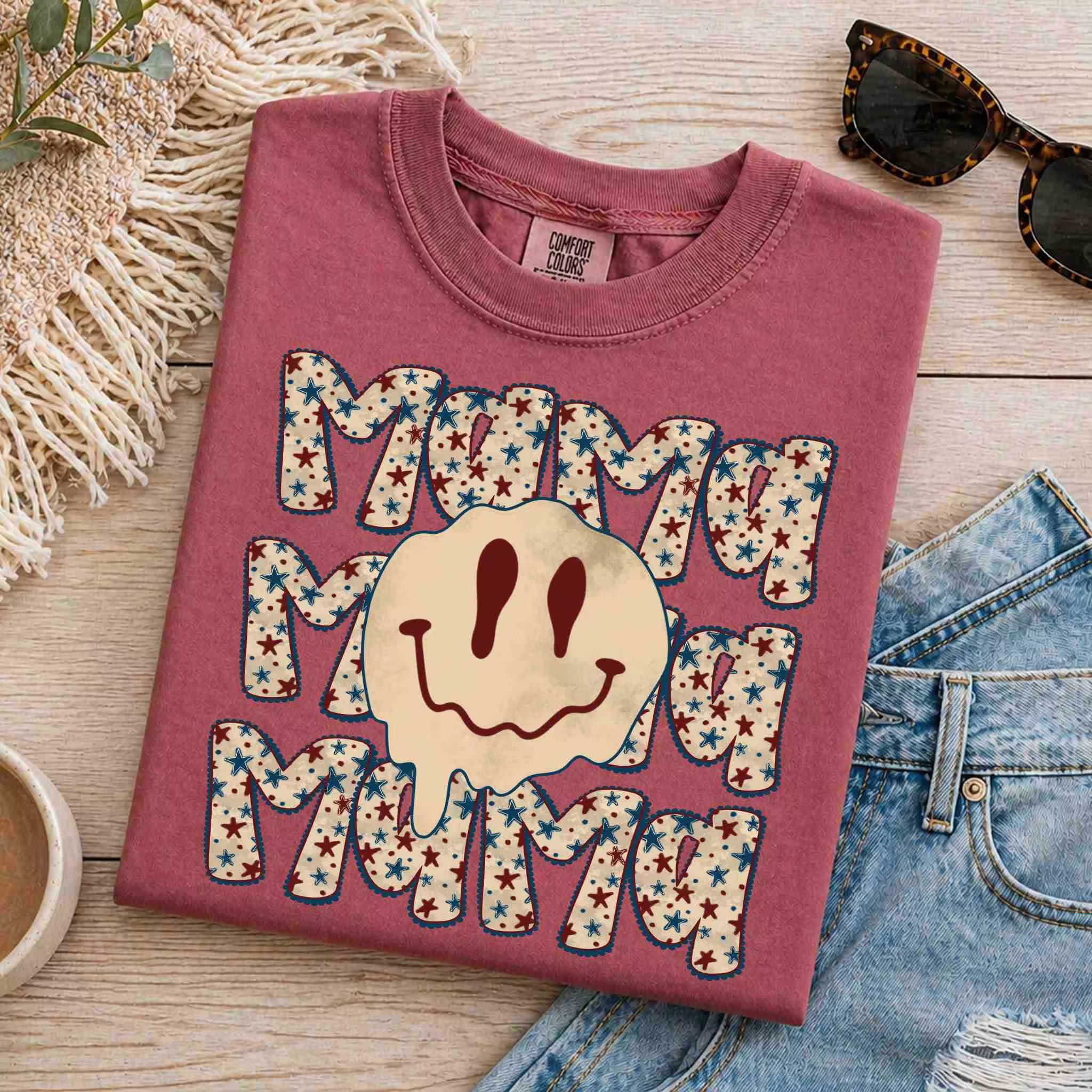 Maroon t-shirt with 'Mama' text design on a wooden surface with denim jeans and sunglasses.