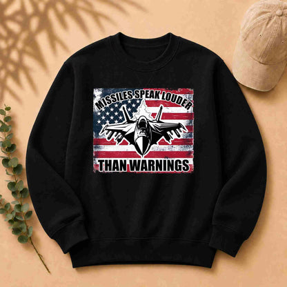 Black sweatshirt with American flag graphic and text on a beige surface with a cap and leaves.