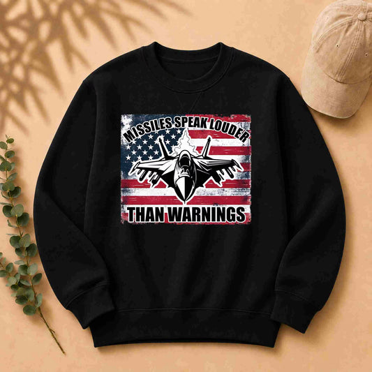 Black sweatshirt with American flag graphic and text on a beige surface with a cap and leaves.