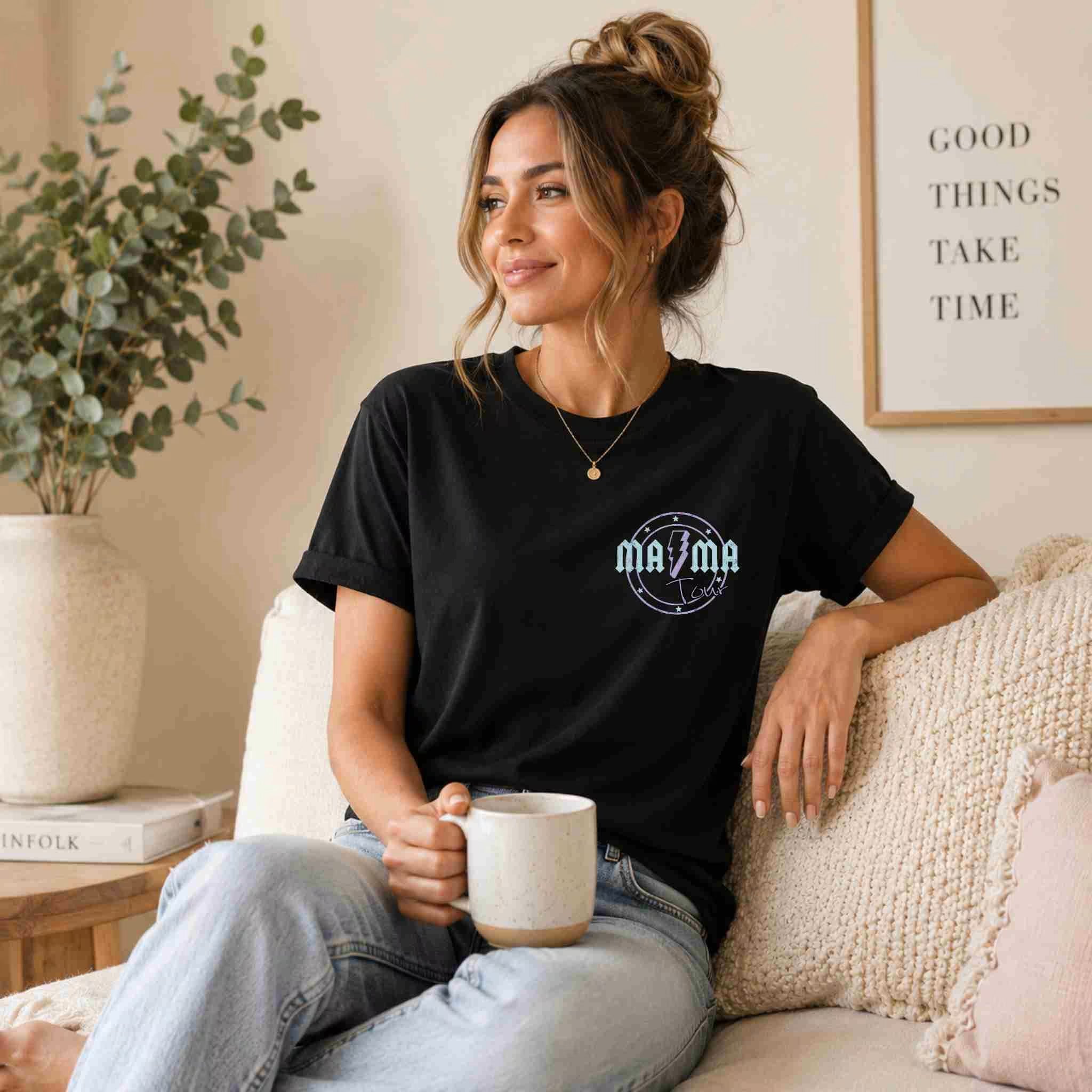Woman wearing a black t-shirt with a logo, sitting on a couch holding a mug.