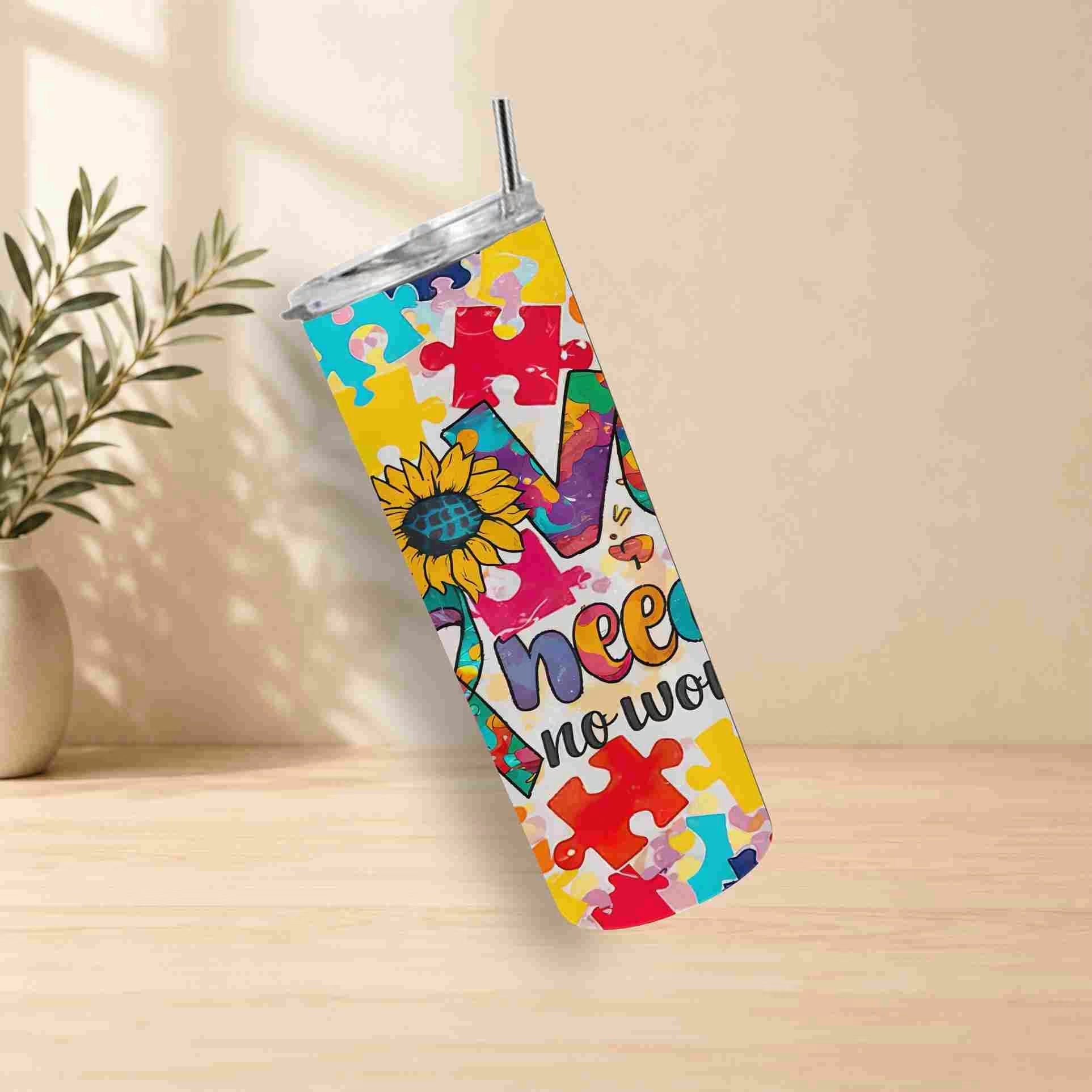 The Autism Awareness Love Needs No Words Tumbler – 20oz by Becca's Banging Designs LLC features a sunflower and puzzle pieces. Shown on a wooden surface beside a potted plant, it's the perfect autism support gift.