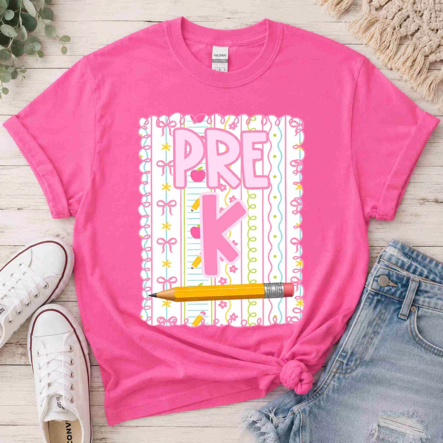 Pink t-shirt with 'PRE K' design on a wooden surface with shoes and shorts.