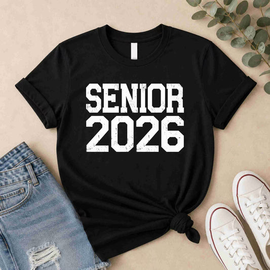Black t-shirt with 'Senior 2026' text on a beige surface with jeans and shoes.