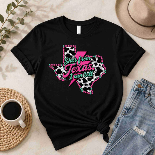 Black t-shirt with Texas design and text on a light surface with coffee, jeans, and hat.