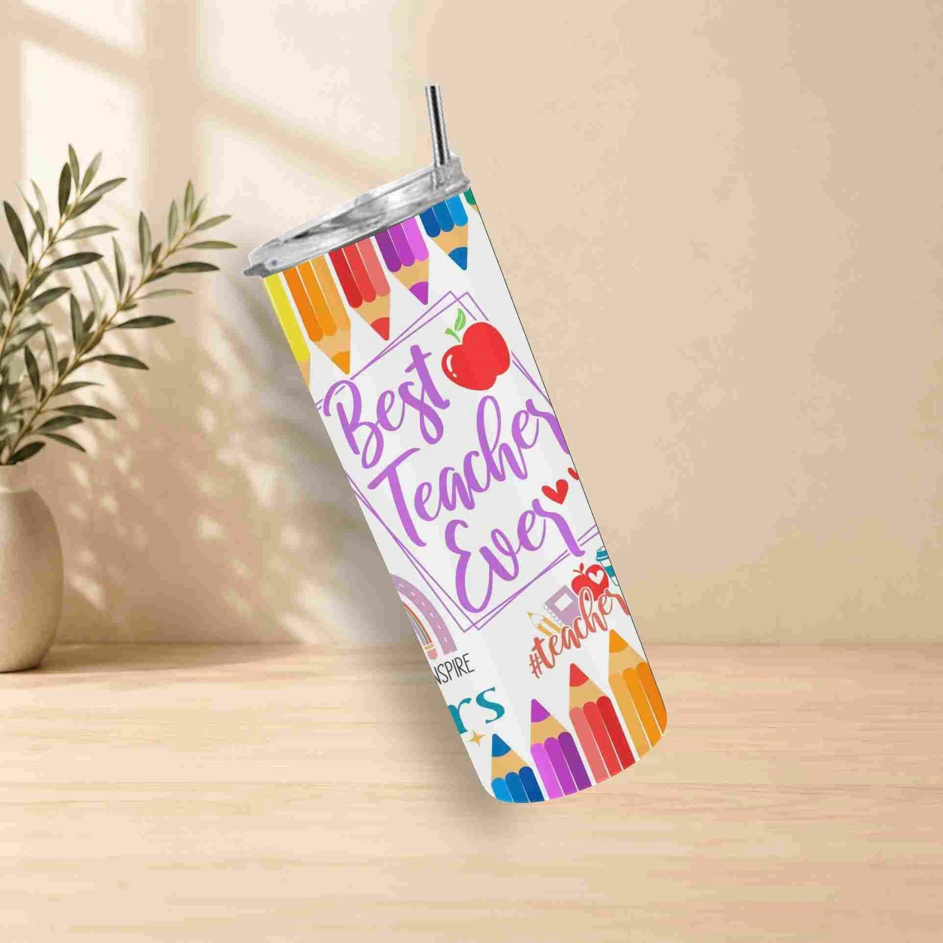 The Best Teacher Ever | 20oz Tumbler features colorful pencils, an apple illustration, and "Best Teacher Ever" text. Ideal as a teacher gift, it's shown on a wooden surface with a plant and beige wall in the background.