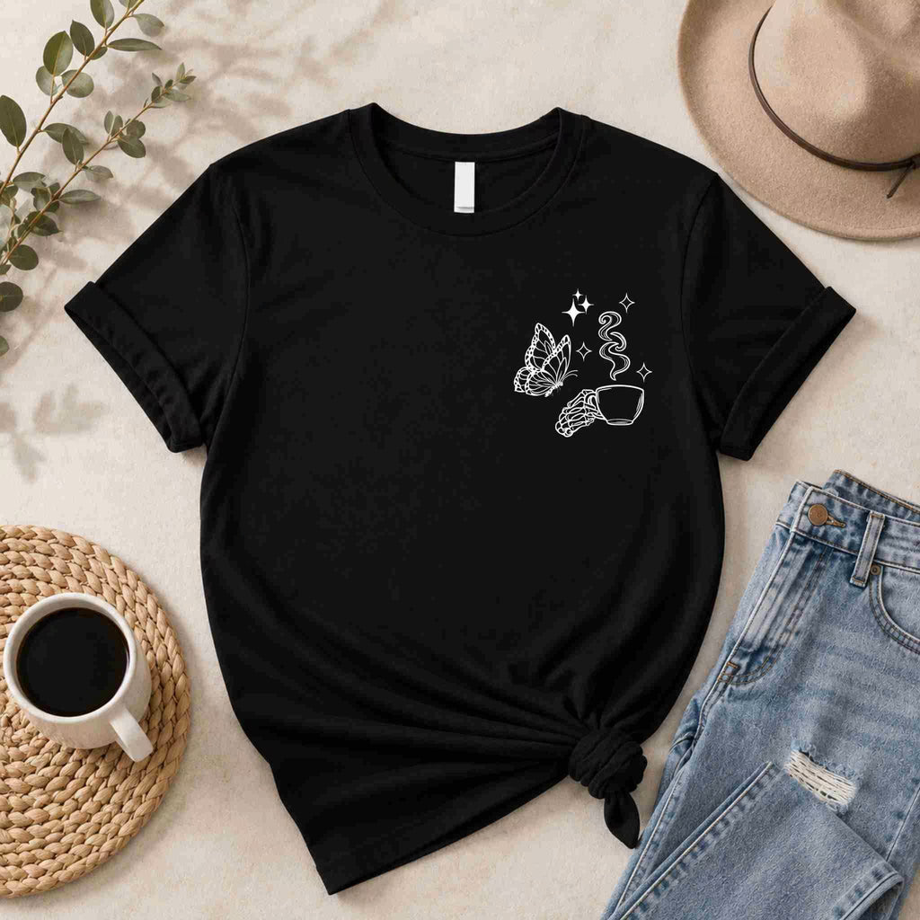 The Undercaffeinated Moms Club Shirt by Becca's Banging Designs LLC features a white minimalist butterfly, hand with a coffee cup, and stars—perfect for cute t-shirt outfits and women's graphic tee collections. Styled with coffee cup, plant, hat, and jeans.