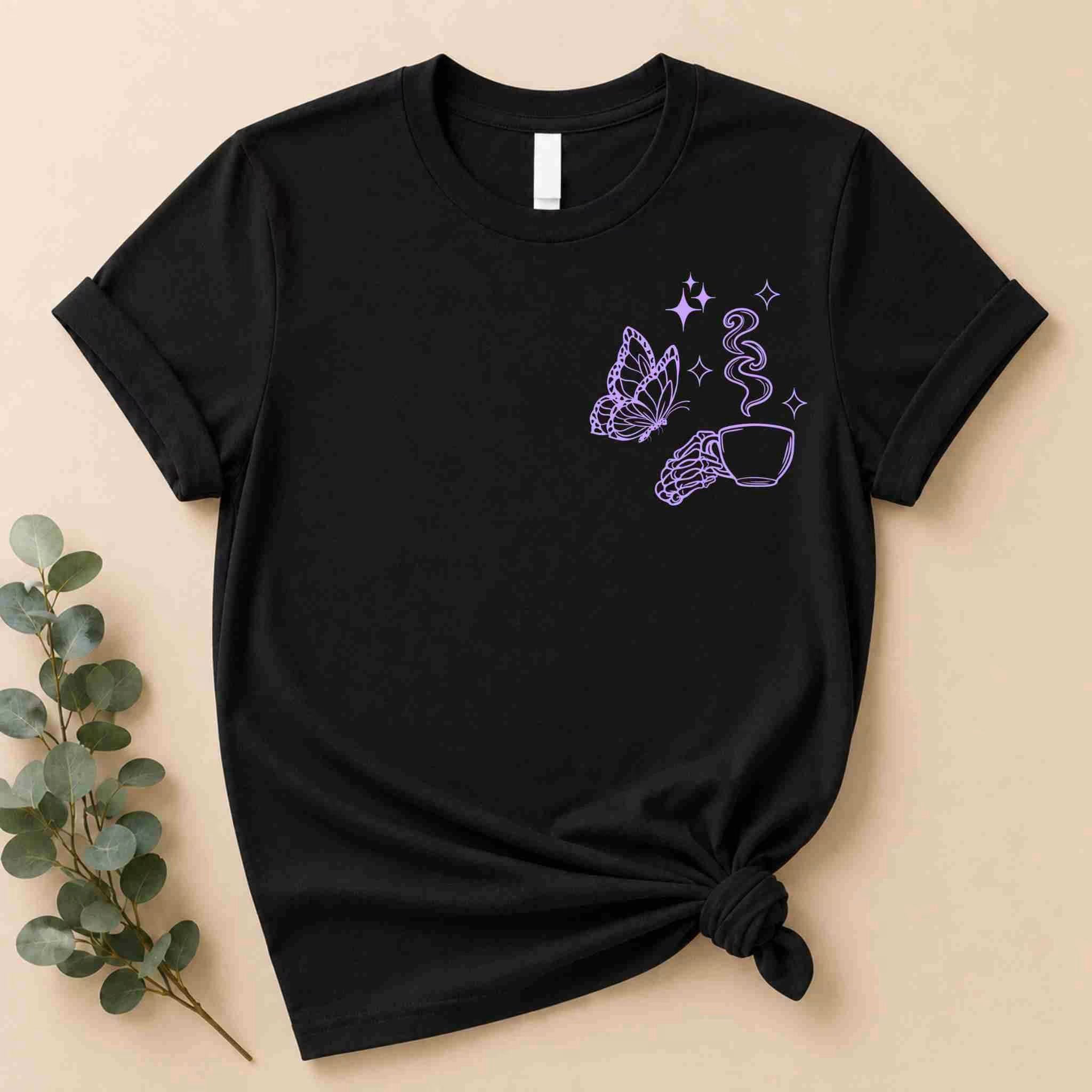 The Undercaffeinated Moms Club Shirt by Becca's Banging Designs LLC is a black tee with a purple line art butterfly, hand holding a teacup, steam, and stars on the upper left chest—perfect for cute outfits or tired moms. Laid flat with knotted hem.