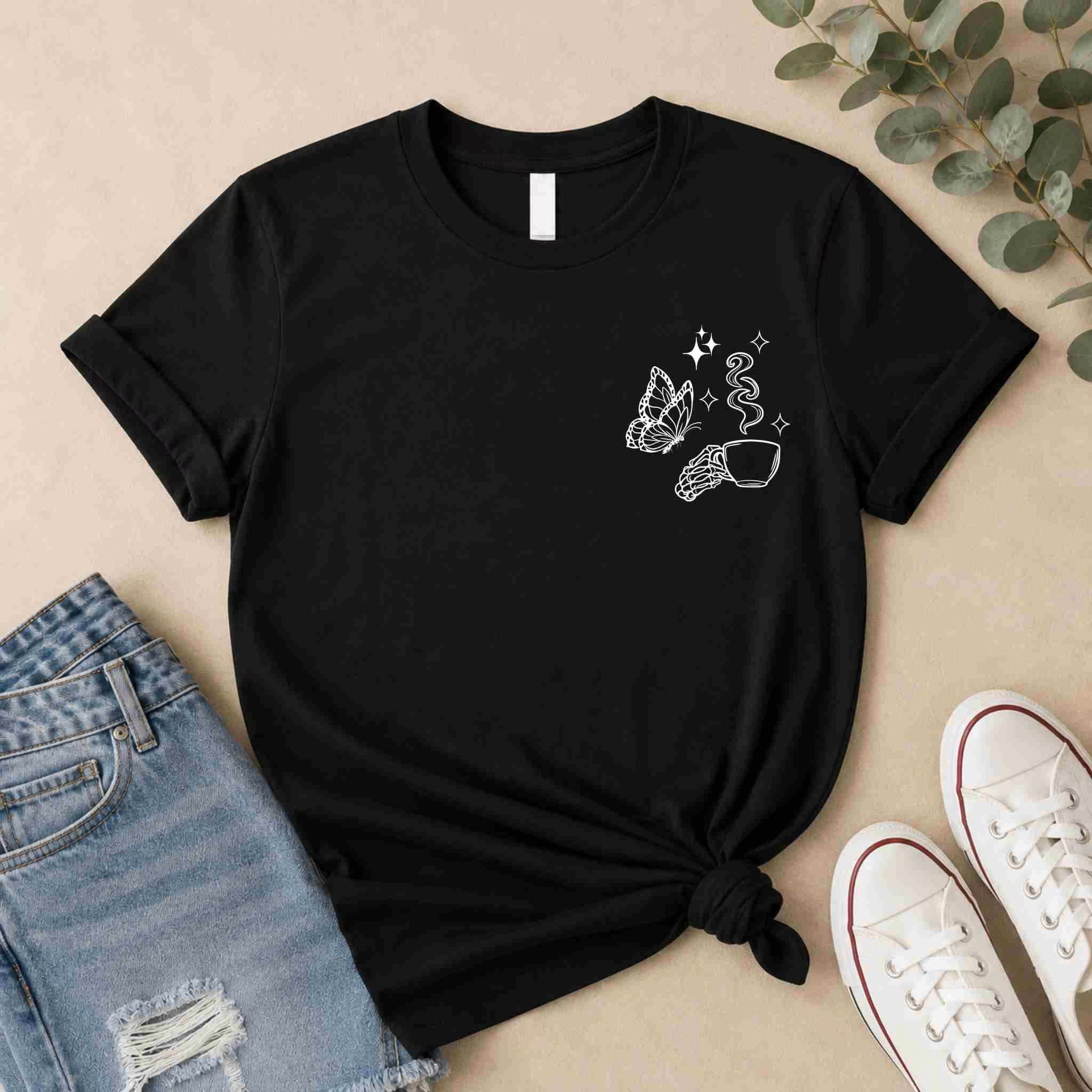 The Undercaffeinated Moms Club Shirt by Becca's Banging Designs LLC, a black women's graphic tee with white line art of a butterfly, crystal, and sparkles, is styled with denim shorts and sneakers—perfect for cute mom outfits.