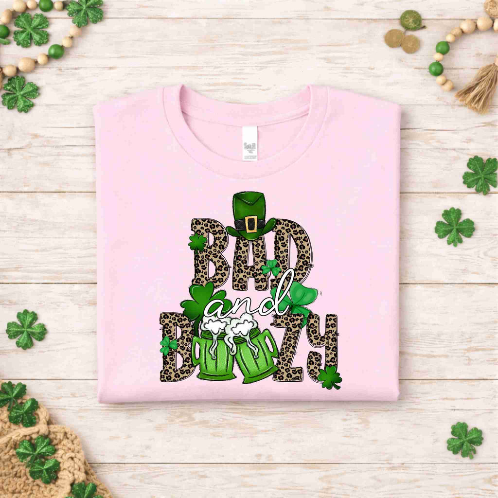 St. Patricks Day shirt featuring Bad & Boozy design with leopard print, shamrocks, and beer mugs on light pink fabric.