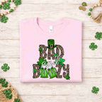 St. Patricks Day shirt featuring Bad & Boozy design with leopard print, shamrocks, and beer mugs on light pink fabric.