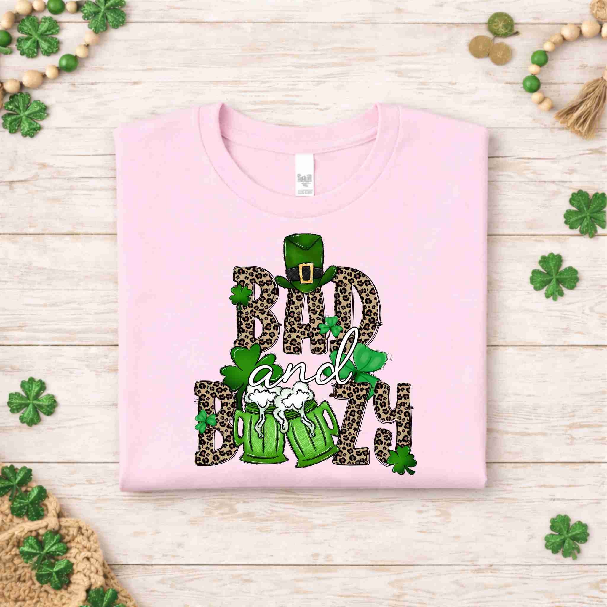 St. Patricks Day shirt featuring Bad & Boozy design with leopard print, shamrocks, and beer mugs on light pink fabric.