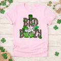 St. Patricks Day shirt featuring 'Bad and Boozy' graphic with leopard print, shamrocks, and beer mugs on light pink tee.