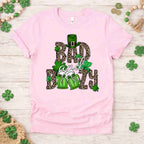 St. Patricks Day shirt featuring 'Bad and Boozy' graphic with leopard print, shamrocks, and beer mugs on light pink tee.
