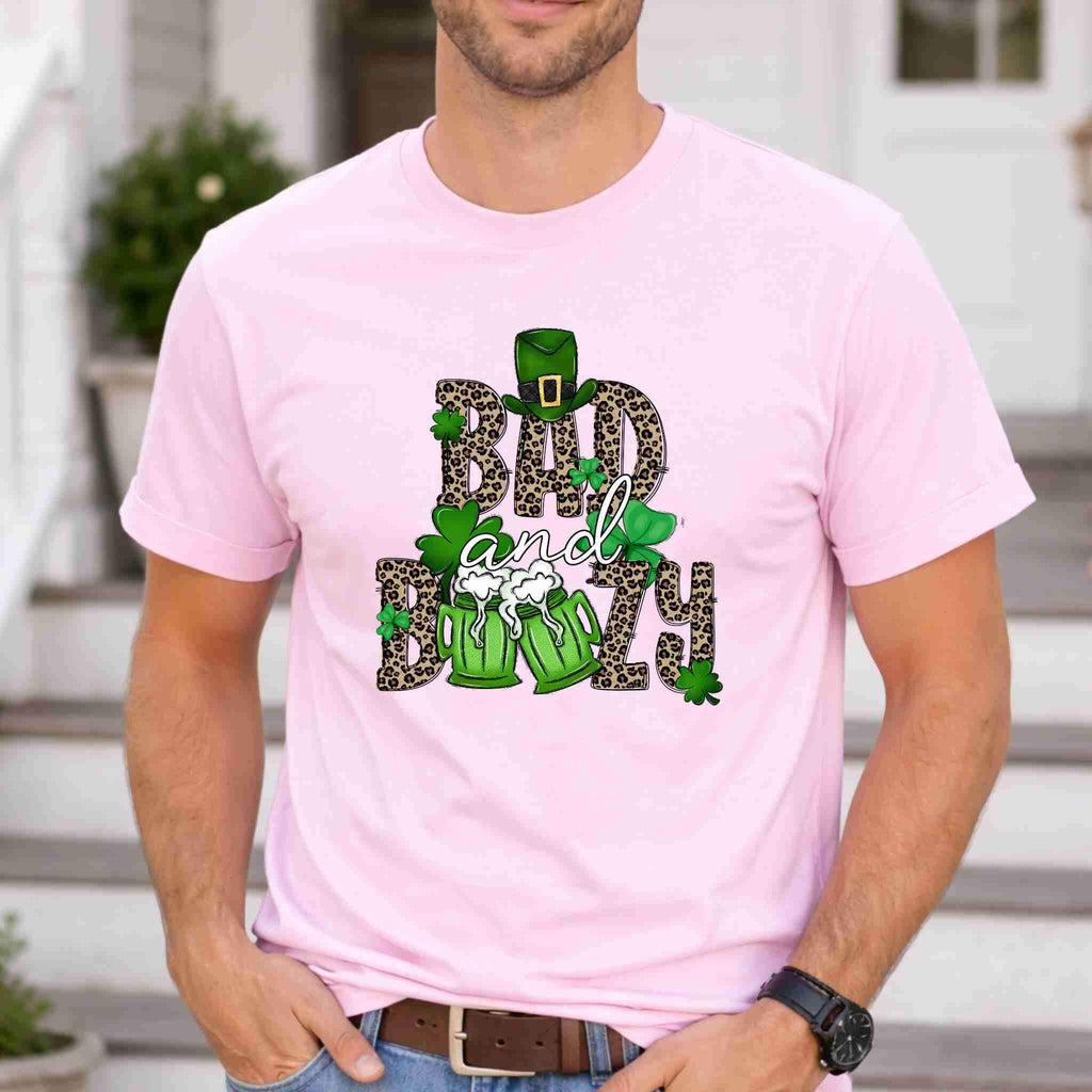 St. Patricks Day shirt featuring Bad & Boozy graphic with leopard print and shamrocks on light pink background.