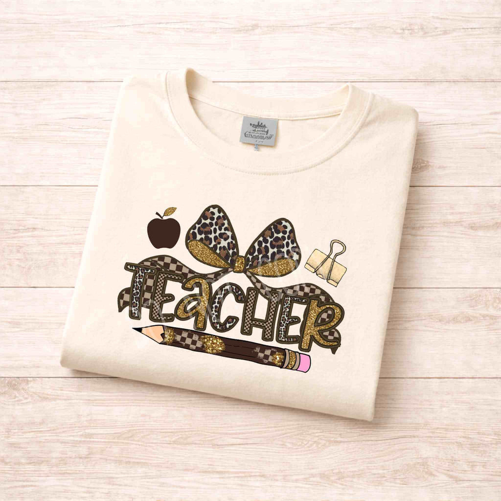 Leopard Love Teacher T-Shirt featuring a leopard print bow, apple, pencil, and paperclip design on a soft beige background.