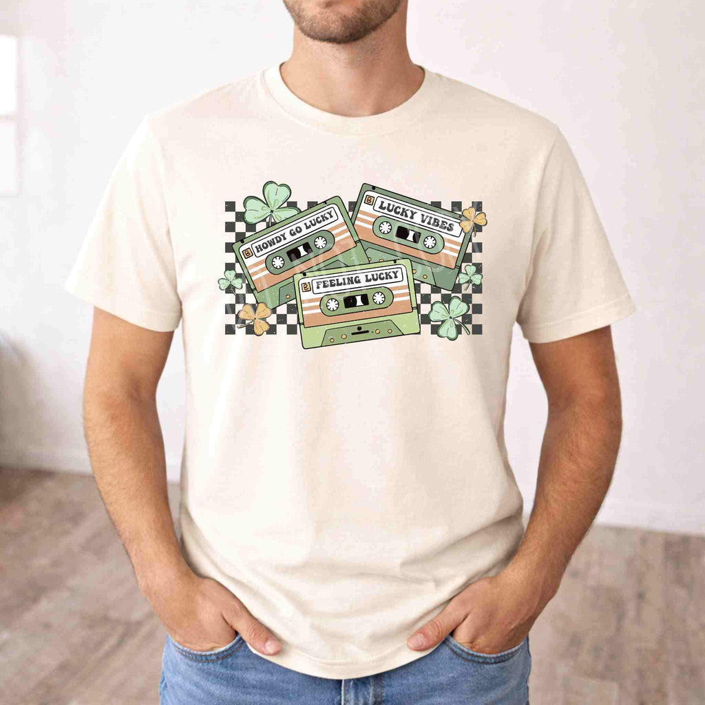 St. Patricks Day shirt featuring retro cassette graphic with shamrocks and checkered accents on a cream tee.
