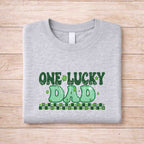 St. Patricks Day One Lucky Dad graphic tee on a wooden background for family celebrations.