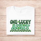 St. Patricks Day One Lucky Aunt shirt with green lettering and shamrock designs on a white background.