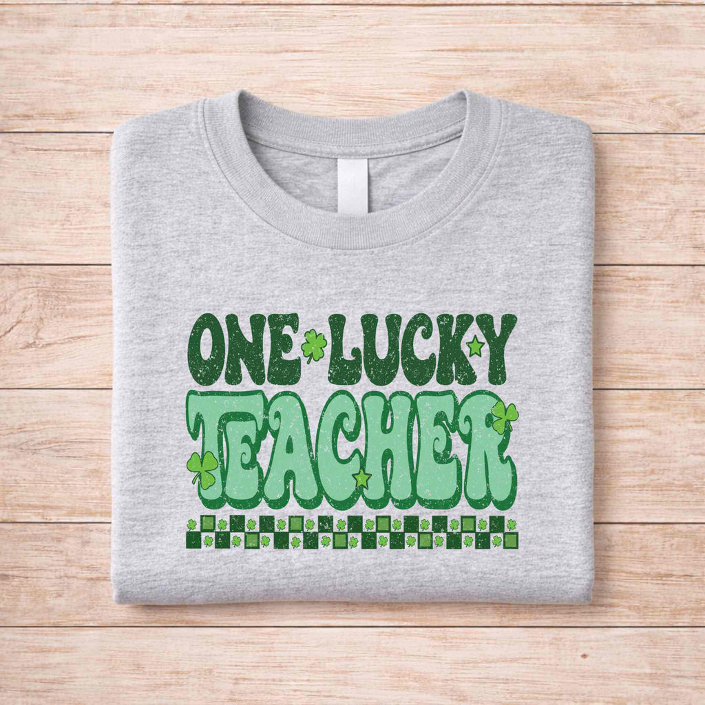 St. Patricks Day Teacher T-Shirt featuring playful 'One Lucky Teacher' shamrock design on a gray background.
