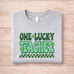 St. Patricks Day Teacher T-Shirt featuring playful 'One Lucky Teacher' shamrock design on a gray background.