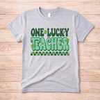 St. Patricks Day Teacher T-Shirt featuring 'One Lucky Teacher' graphic with shamrocks on a gray tee.